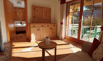A cozy living space with wooden furniture and large windows. The light gently falls onto the floor, creating an inviting atmosphere.