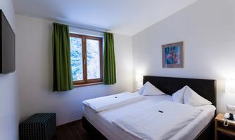 A cozy bedroom with a double bed and green curtains. Daylight falls on the furniture through the window.
