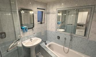 A modern bathroom with a shower, a bathtub, and a sink. The walls are brightly tiled, and a carpet with colorful patterns lies on the floor.