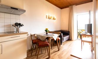 A cozy apartment with a small kitchen and a dining area. The room is bright and has large windows that lead to a balcony.