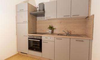A modern kitchen with gray cabinets and a wooden countertop. It is equipped with a stove, an oven, and a sink.
