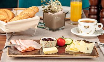 A rich breakfast set with cold cuts, cheese, butter, fresh tomatoes, and cucumbers. Accompanied by a coffee and a glass of fresh-squeezed juice.