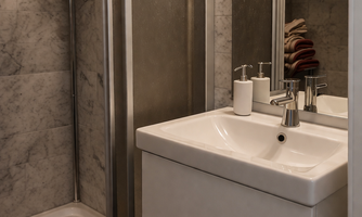 A modern bathroom with a shower and a sink. The walls are lined with gray marble and there are towels in various colors ready.
