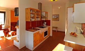 A bright and friendly kitchen with wooden shelves and modern appliances. The space is well-lit and invites cooking.