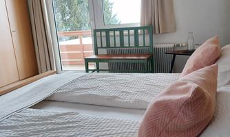 A bedroom with a large bed and pink pillows. Through the window, there is a view of a balcony and trees.