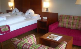 A cozy hotel room with two beds and a seating area. The furniture is designed in modern, colorful fabrics.