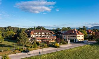 A classic hotel building surrounded by lush greenery and a clear blue sky. The road runs directly in front of the hotel, which is located in a tranquil landscape.