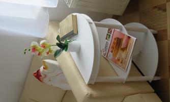 An elegant white side table next to a beige sofa. On the table sits a small plant and some books as well as a magazine.