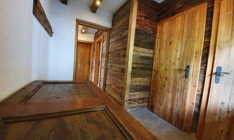 A bright hallway with rustic wooden doors and a wooden cupboard. The walls are adorned with wooden paneling, creating a cozy atmosphere.