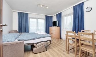 A bright, modern accommodation with a bed, a dining area, and large windows. The decor feels welcoming and cozy.