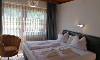 A modern bedroom with a large bed and cozy pillows. Next to the bed is a stylish armchair and large windows let in plenty of light.
