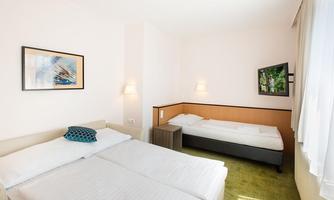 A bright room with two beds and a television. The walls are painted in soft colors and a picture decorates the wall.