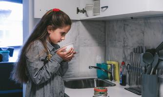 A girl with long hair holds a bowl in the kitchen. She looks thoughtfully at the contents of the bowl.