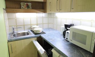 A small kitchen with modern appliances. There is a sink, a refrigerator, and a microwave on a dark countertop.