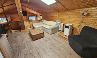 A cozy living space with wooden paneling and a skylight. There is a sofa, an armchair, and a table in the center.