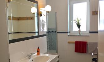 A modern bathroom with a sink and a shower. Bright colors and a large mirror wall give the room a friendly atmosphere.