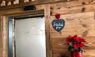 A tastefully decorated entrance with wooden cladding and lovely accents. On a black sign it says "Breakfast 8-9 AM" and a red flower is in a pot.