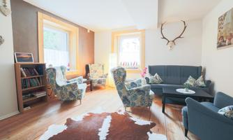 A cozy living room with modern furniture and a wooden floor. The walls are painted in warm colors and there is a large bookshelf.