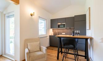 A modern kitchen with a small dining area and a cozy armchair. The room lighting is designed to be friendly and bright.
