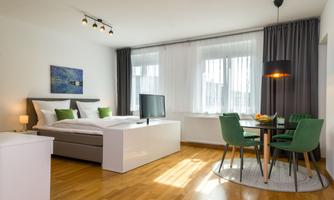 A modern room with a double bed, a television, and a dining table. Large windows provide plenty of daylight.