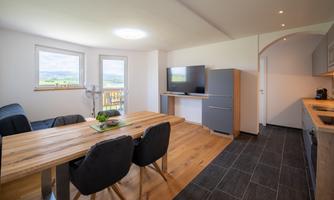 A cozy apartment with a dining area and a modern kitchen. Large windows provide plenty of daylight and a beautiful view of the landscape.