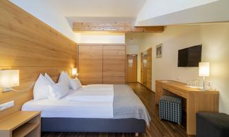 A modern hotel room with a large bed and wooden paneling. There is a television, nightstands, and a small seating area.