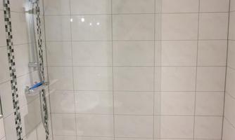 A modern shower with white tiles and a clear sliding glass door. The floor is equipped with gray tiles.