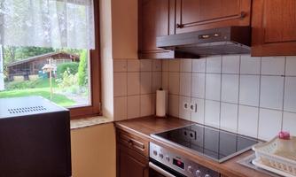 A modern kitchen with wood cabinets and a cooktop. A beautiful garden with a shed is visible through the window.