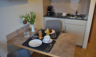 A small dining area with a beautifully set table. In the background, there is a kitchenette with cooking equipment and a coffee machine.