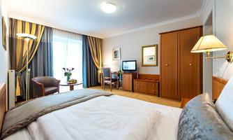 An elegant hotel room with a comfortable bed and a desk. Large windows let in plenty of light and create a pleasant atmosphere.
