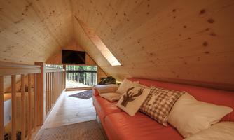 A cozy living area in the attic with an orange sofa and cushions. Large windows provide a view of the outside and let in plenty of light.