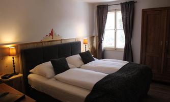 A cozy bedroom with a large double bed and soft pillows. The room has wooden elements and windows with curtains that provide pleasant light.