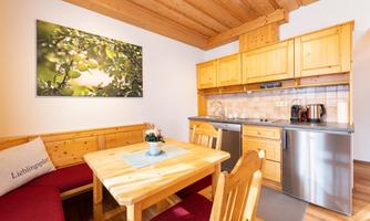 A cozy kitchen with wooden furniture and a dining table. A picture of green apples hangs on the wall.