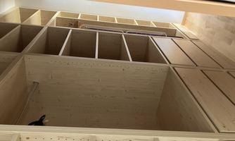 A modern wardrobe made of light wood with open shelves and drawers. The room is tidy and well-organized.