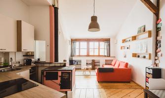 A cozy apartment with an open kitchen and a bright living area. The orange sofa adds a friendly accent to the room.