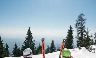 Two skiers are sitting in the snow, enjoying the view of the mountains. The sun is shining in the clear blue sky.