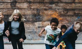 A group of happy children are running and playing in front of a wooden wall. They are laughing and having fun together.