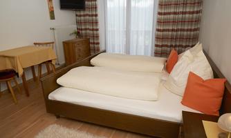 A cozy room with a double bed and colorful cushions. Pleasant atmosphere with a table and chair as well as natural light through the windows.