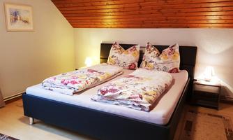 A cozy bedroom with a double bed and colorful bedding. The wooden ceiling and soft lighting create an inviting atmosphere.