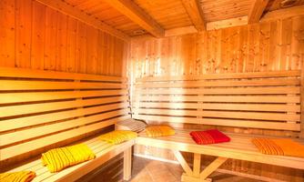 A cozy sauna room made of wood with several benches. Colorful towels are placed on the benches.