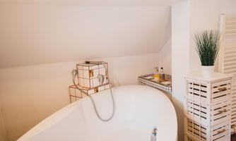A modern bathroom with a freestanding bathtub. In the background, elegant storage baskets and a plant can be seen.