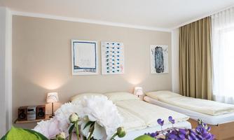 A bright and cozy bedroom with two beds. Modern artworks hang on the wall, and fresh flowers adorn the table.
