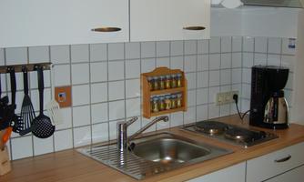 A modern kitchen with white cabinet doors and a wooden countertop. There is a sink, cooking utensils, and a coffee maker.
