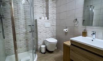 A modern bathroom with a shower, a sink, and a toilet. The walls are tiled in neutral tones, and there are wood accents.