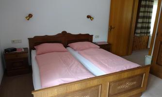 A simple bedroom with two single beds and pink bedding. The room has wooden paneling and a door to an adjacent room.