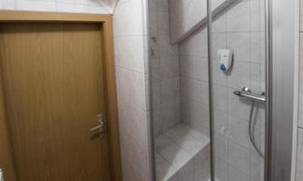 A modern bathroom with a shower and a wooden container. The walls are tiled and the bathroom has a bright, friendly style.