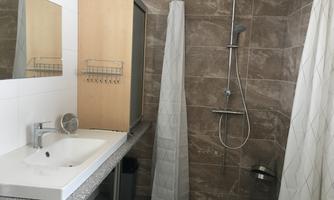 A modern bathroom with a shower and a sink. The walls are covered with brown tiles, and there is a mirror and a storage cabinet.