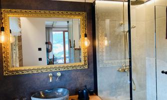A modern bathroom with an elegant golden mirror frame and a stylish shower. On the wooden shelf, there is a decorative sink and colorful towels are visible.