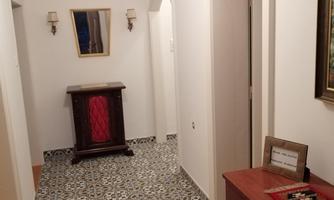 A bright hallway with a beautiful tile pattern. Pictures hang on the walls, and there is a tasteful dresser.