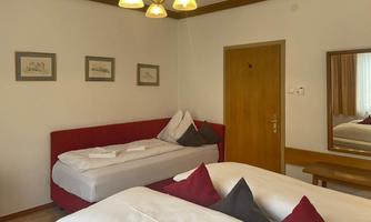 A simple bedroom with two beds, a red sofa, and a mirror. There is a wooden chair and a door to the other side of the room.